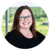 Headshot shows Liz Gross smiling wearing a black shirt and bright blue glasses while smiling at the camera Headshot shows Liz Gross smiling wearing a black shirt and bright blue glasses while smiling at the camera